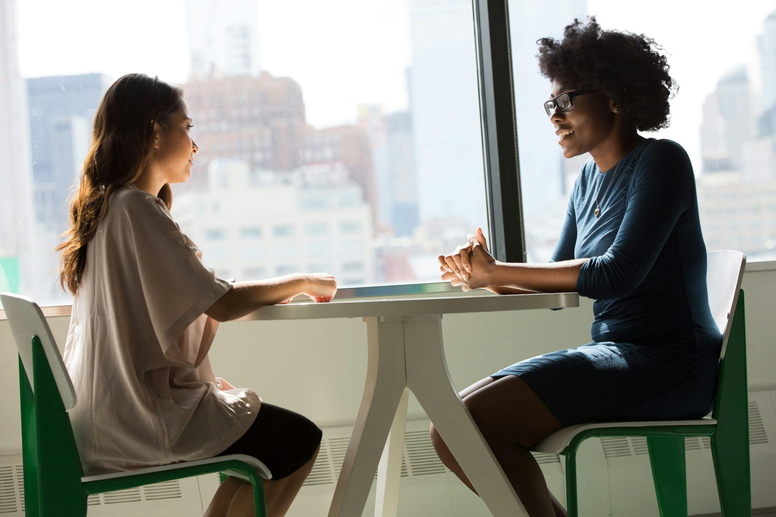 Duas mulheres, sentadas de frente em uma mesa, conversando